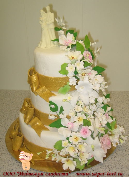 Трехъярусный белый свадебный торт с большим красивым букетом и золотыми лентами с фигуркой жениха и невесты из шоколада